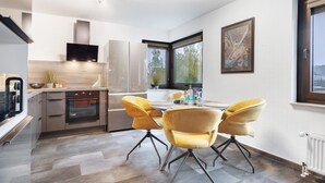 Une cuisine moderne dotée d’appareils électroménagers intégrés, un coin repas avec des chaises jaunes et une grande fenêtre laissant entrer la lumière naturelle.