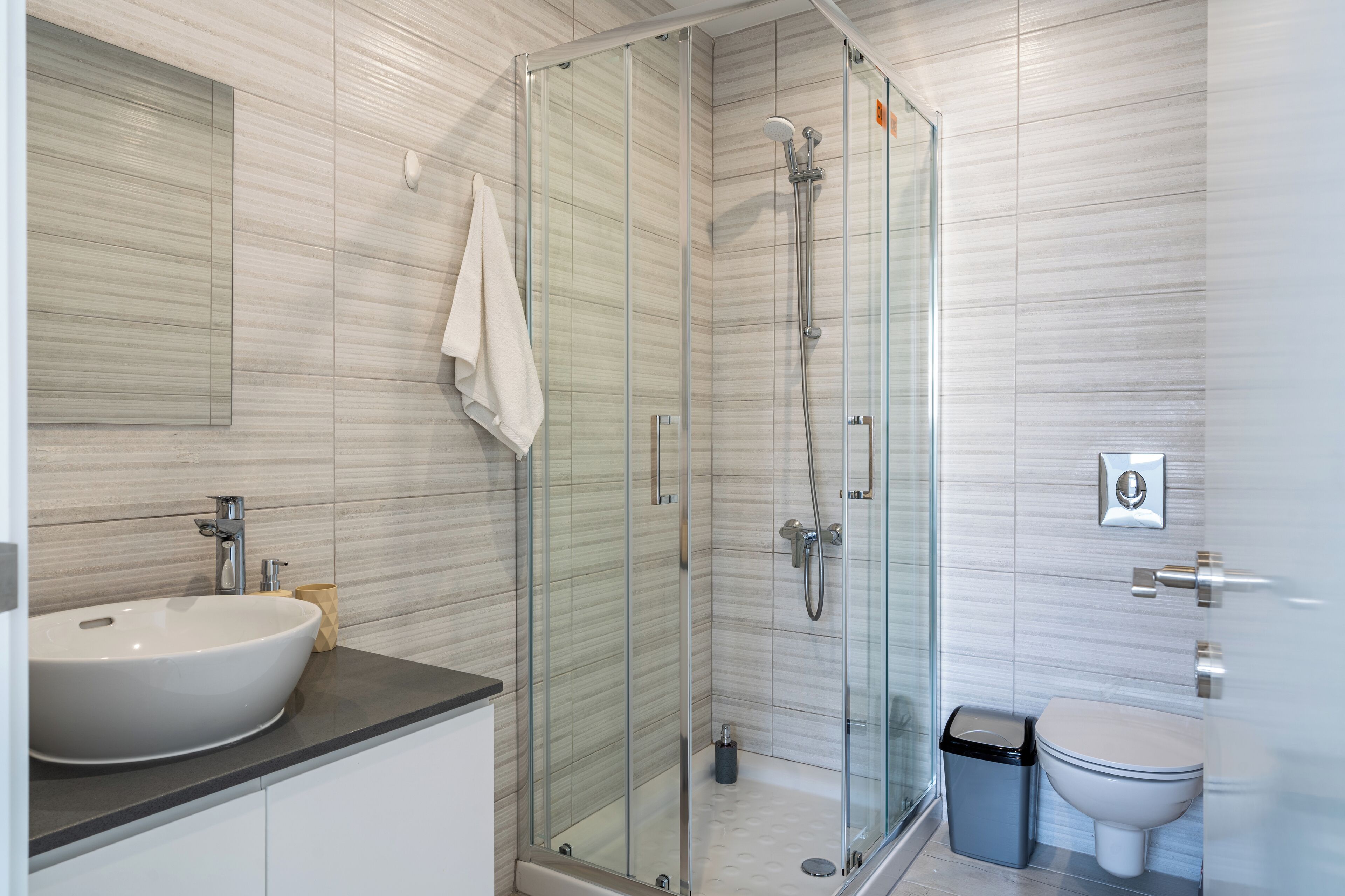 Un baño moderno con ducha de vidrio, un lavabo blanco y un inodoro.