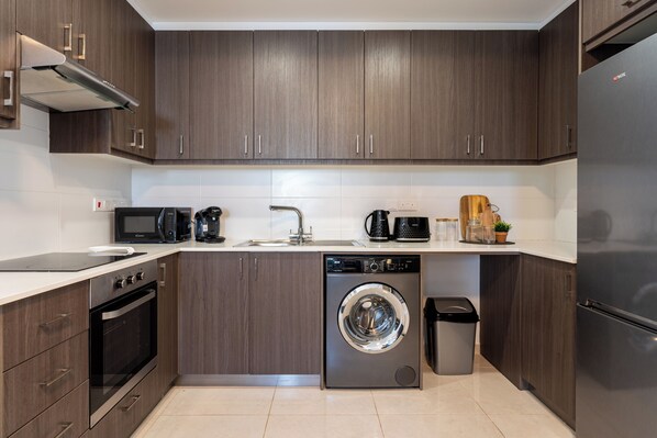 Una cocina moderna con gabinetes de madera oscura, horno integrado, lavavajillas, microondas y refrigerador de acero inoxidable.