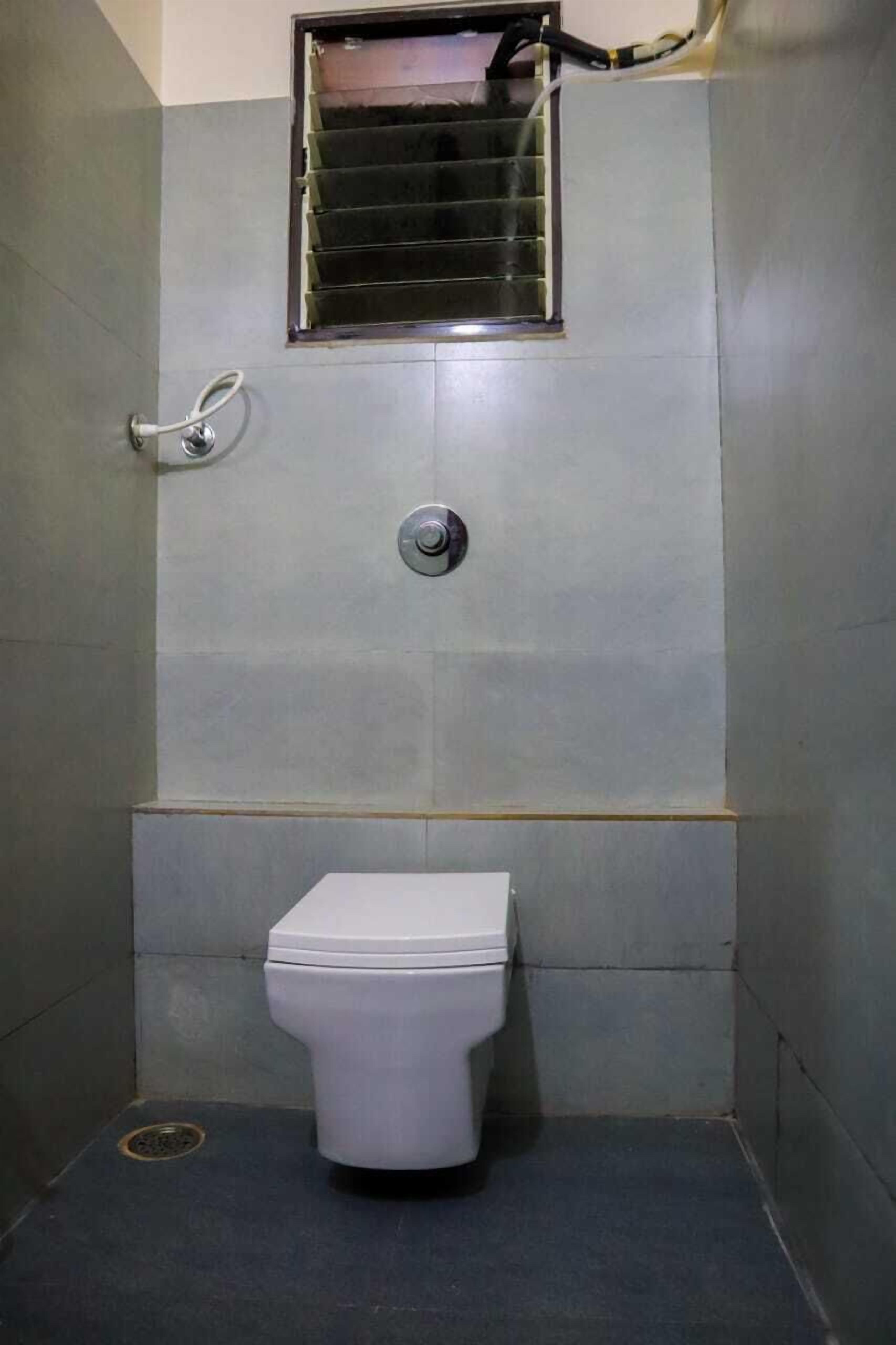 Un baño pequeño con baldosas, que incluye un inodoro, una ventana con reja de metal y un grifo instalado en la pared.