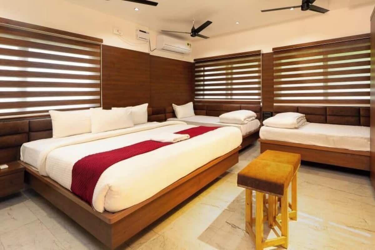 A modern hotel room with a large bed, a smaller bed, a bench, and a desk.