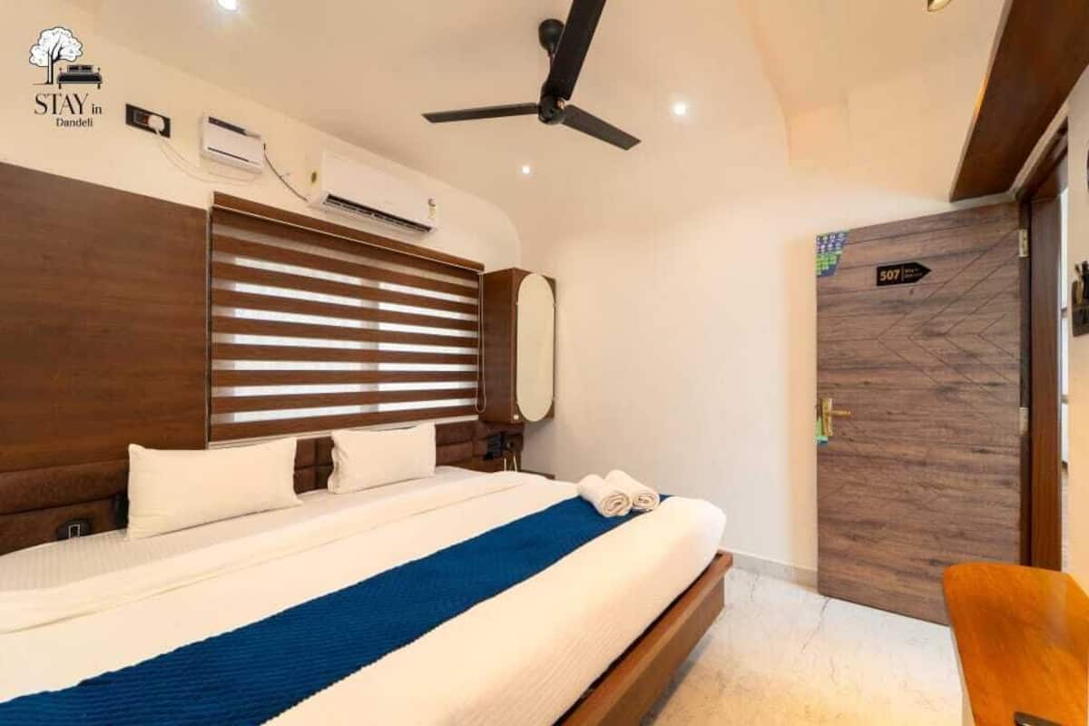 A hotel room with a bed, a ceiling fan, an air conditioning unit, a wooden door, and a sign indicating room number 507.