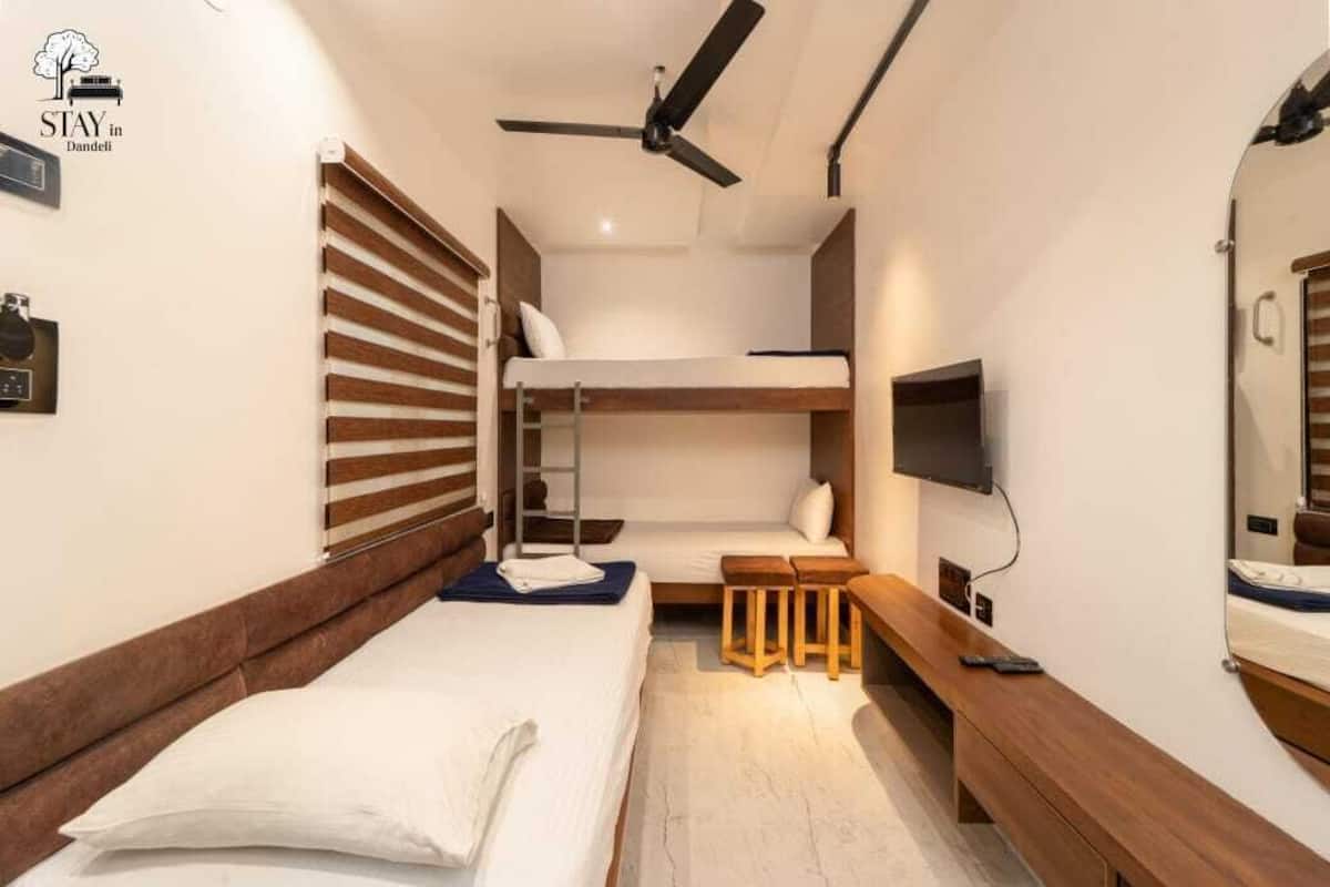 A compact hotel room with a bunk bed, a ceiling fan, a TV, and a wooden bench.