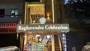 Un immeuble à plusieurs étages, avec une enseigne indiquant « Raghavendra Celebration » à l’entrée.