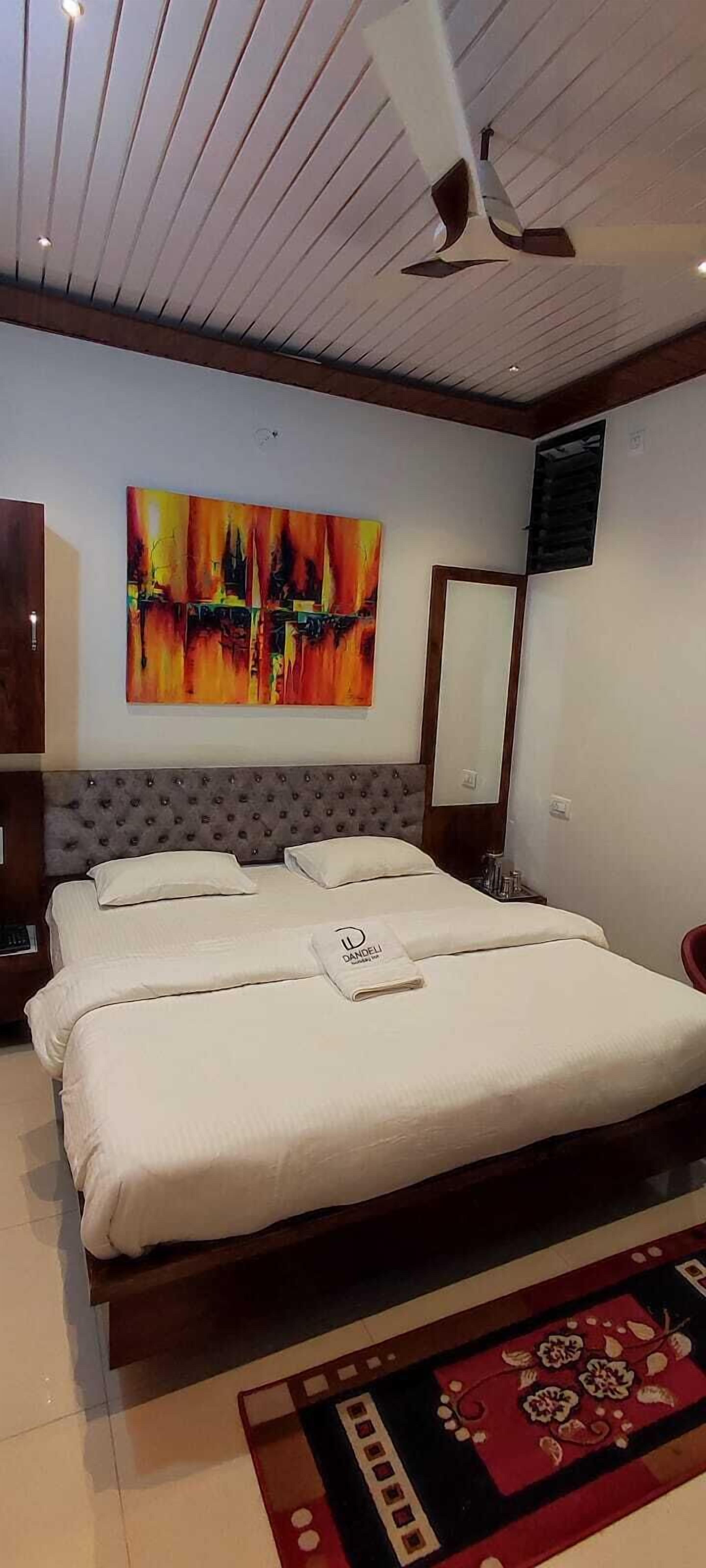 Habitación de hotel con una cama grande, un ventilador de techo, un cuadro en la pared y una alfombra con motivos rojos y negros.