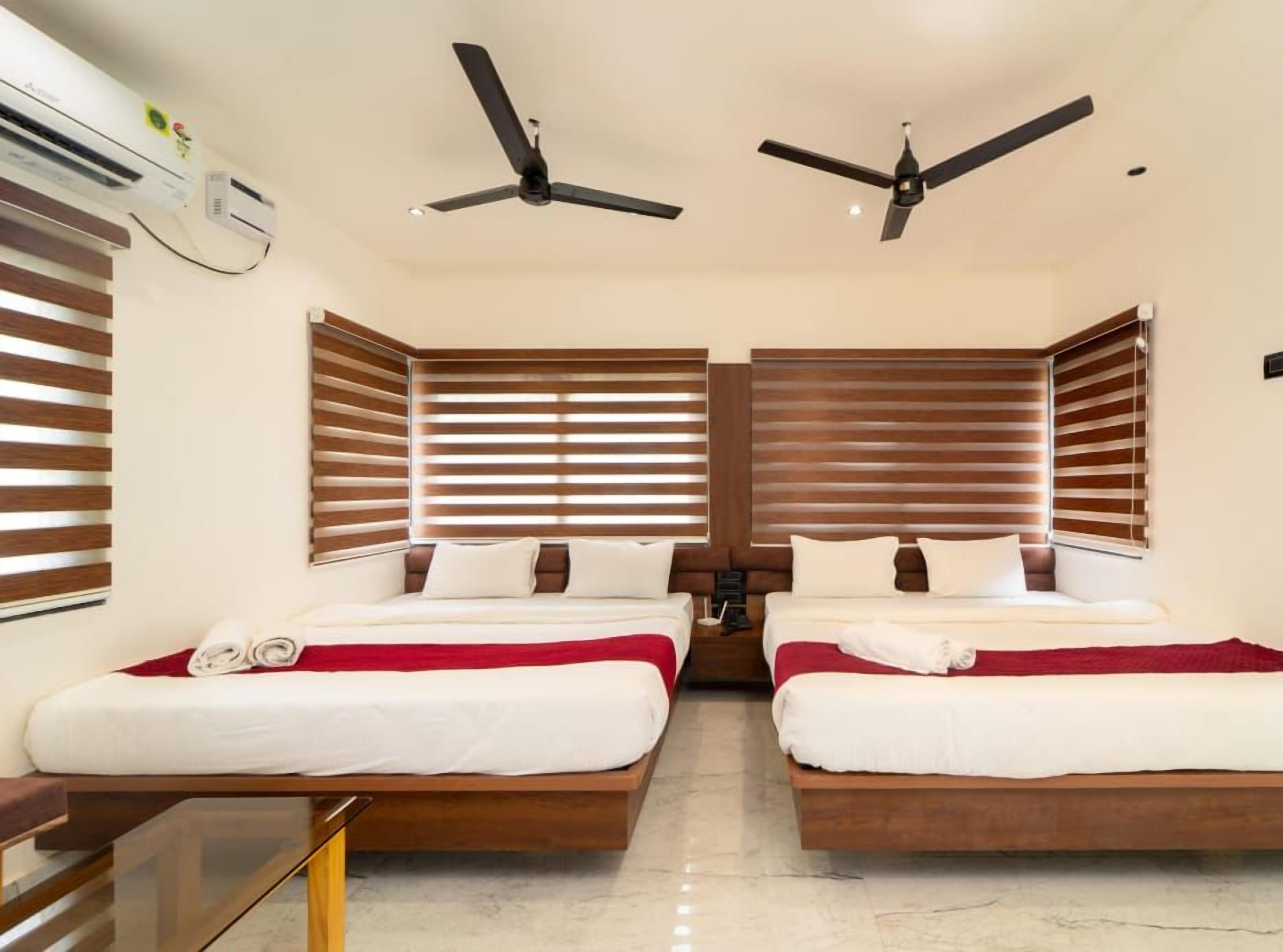 A hotel room with two beds, wooden headboards, ceiling fans, and a minibar.