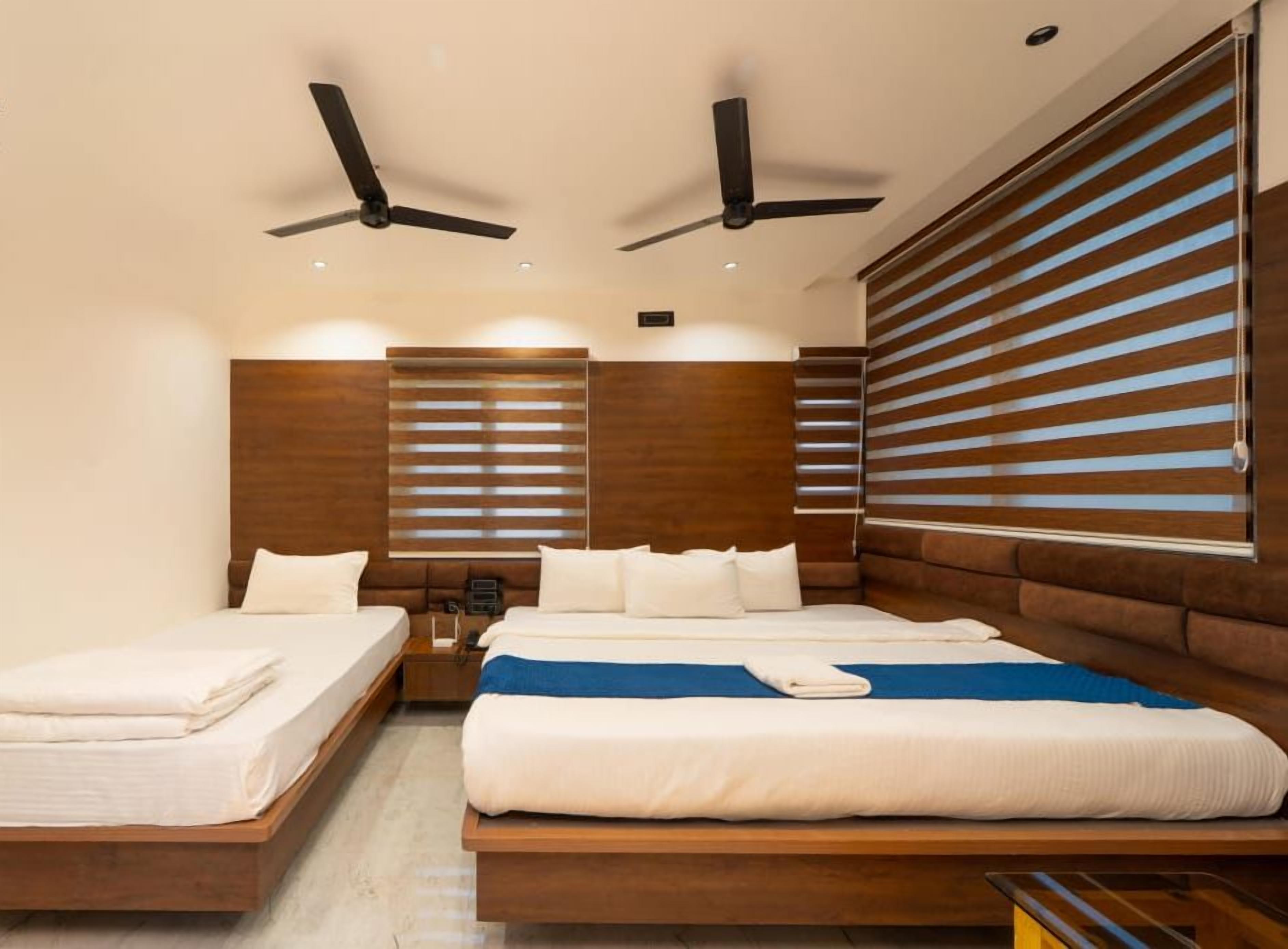 Ein Hotelzimmer mit zwei Betten, Holz-Kopfteilen, Deckenventilatoren und großen Fenstern mit Jalousien.