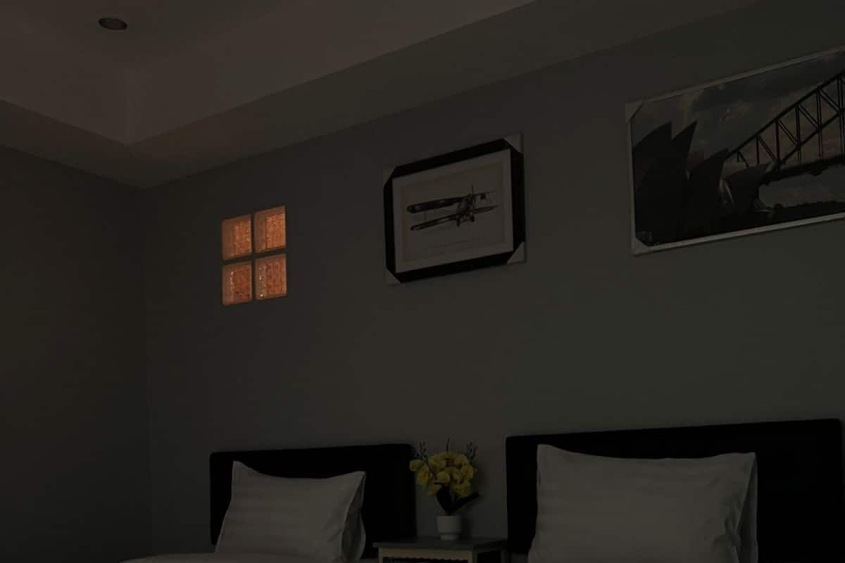 A hotel room with two beds, a nightstand with a vase of flowers, and framed pictures on the wall.