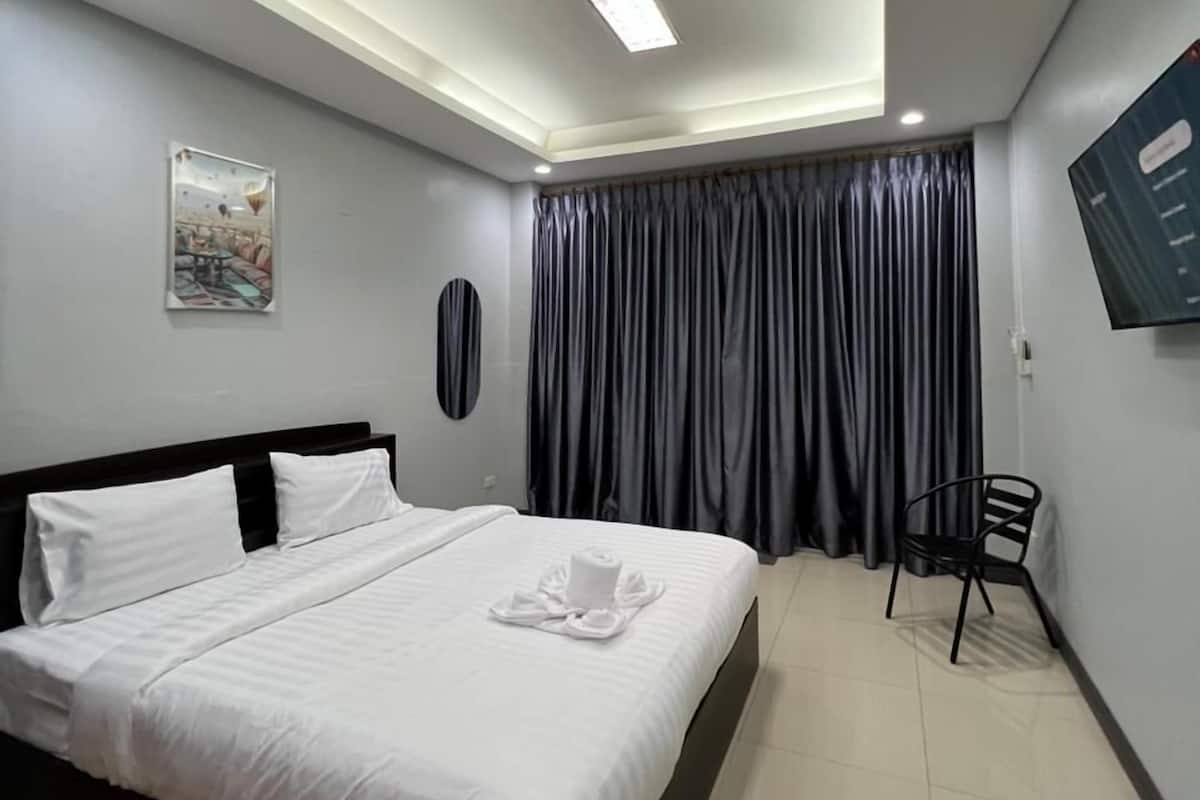 A modern hotel room with a large bed, a flat-screen TV mounted on the wall, and a ceiling light fixture.