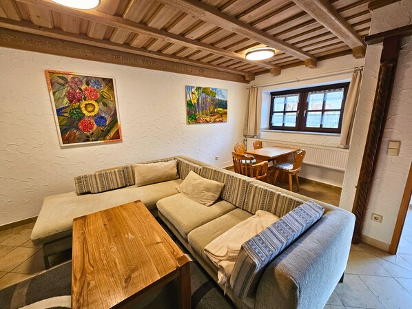 A cozy living room with a wooden ceiling, a sofa, a small wooden table, and two paintings on the wall.