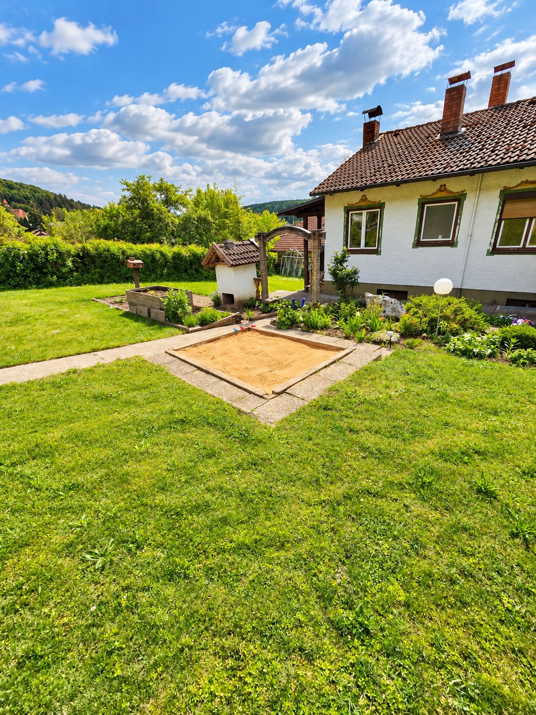 Un jardin bien entretenu, agrémenté d’une terrasse, d’un petit abri de jardin et d’une maison avec un toit en tuiles.