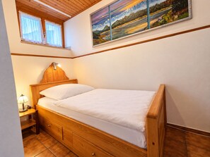 A single bed with a wooden frame and headboard, a bedside table with a lamp, and a window with curtains.
