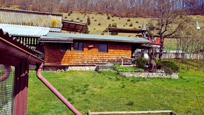 Una casa de fusta rústica amb teulada inclinada, fonamentació de pedra i un petit jardí amb una estàtua.