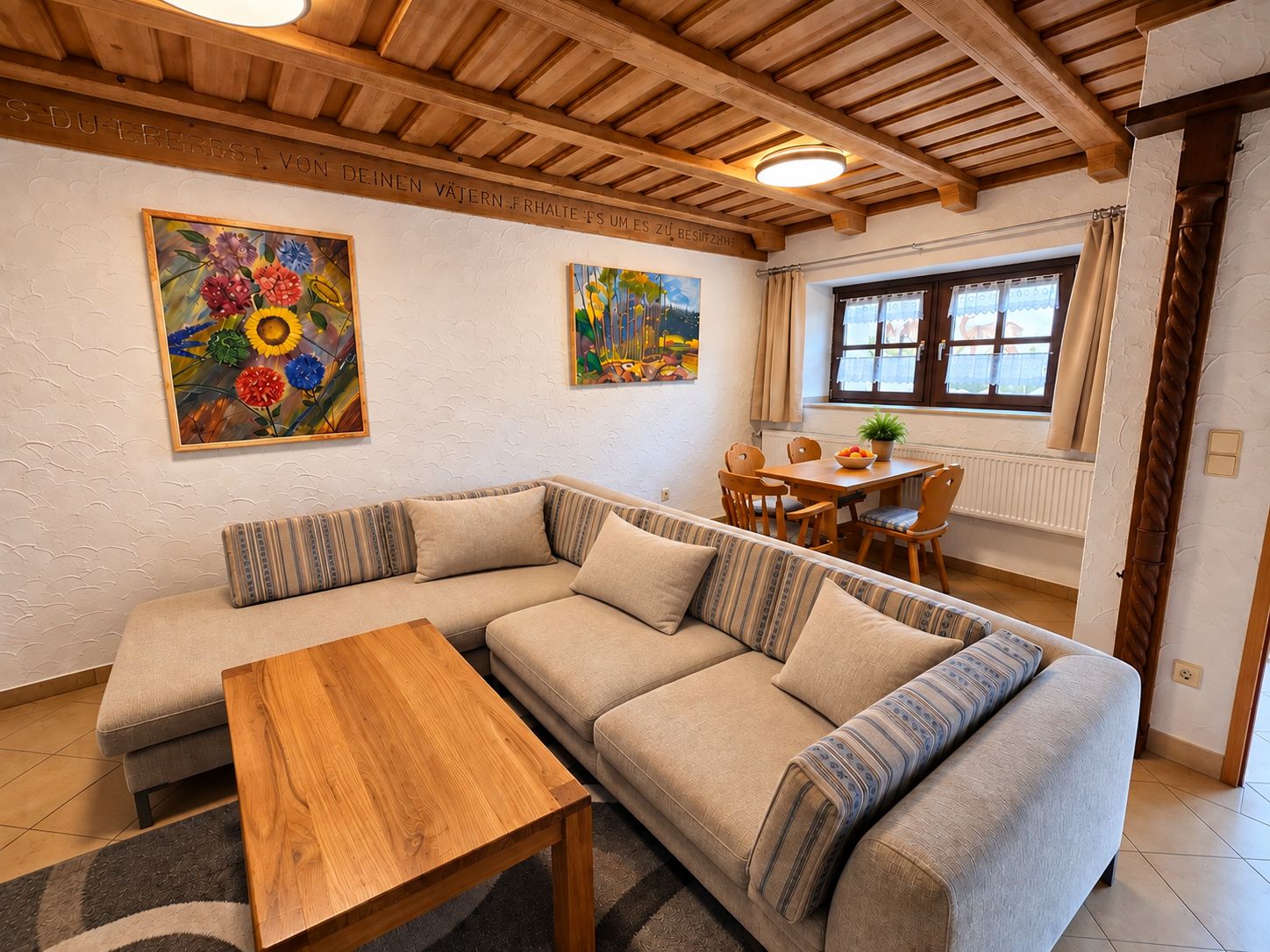 A cozy living room with a wooden ceiling, a sofa, a coffee table, and two paintings on the wall.