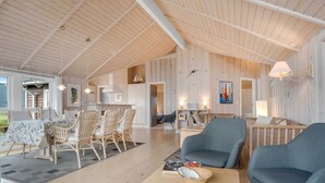 Un espacio habitable amplio con techo alto, paredes de madera y un comedor con sillas de mimbre.