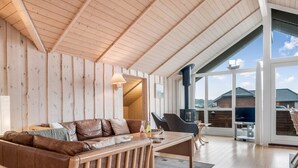 Amplia sala de estar con techo de madera, sofá de cuero, una mesa de centro y un ventanal con vistas al exterior.