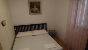Ein ordentlich bezogenes Bett mit weißen Leinen, ein gerahmtes Bild an der Wand und ein kleiner runder Tisch daneben.