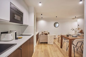 Uma cozinha moderna com forno embutido, uma sala de jantar com mesa e cadeiras de madeira, e um sofá com um espelho acima.