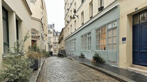 Eine enge Kopfsteinpflasterstraße, gesäumt von Gebäuden mit großen Fenstern und einer blauen Tür auf der rechten Seite.