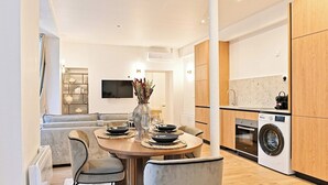 Eine moderne Küche mit integriertem Waschmaschinenanschluss, ein Essbereich mit rundem Tisch und ein Wohnbereich mit Sofa und Fernseher.
