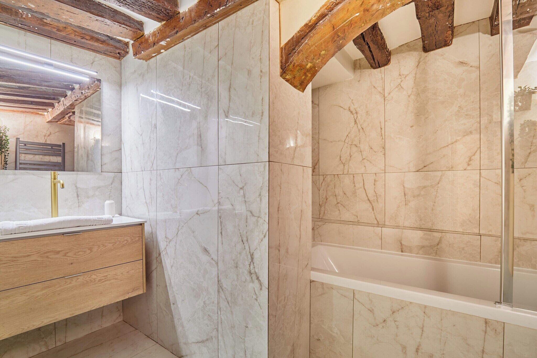 A bathroom with marble walls, a wooden vanity, and a glass shower enclosure.