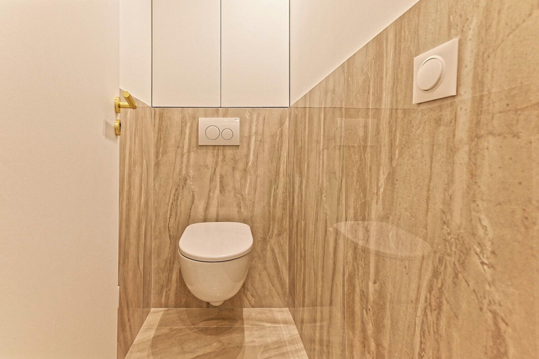 A modern bathroom with a marble wall, a toilet, a control panel, and a flush button.