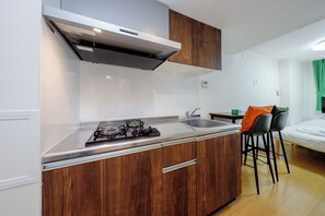 A compact kitchen with a gas stove, a sink, and wooden cabinets. - Oakiville Nezu (Tokyo)