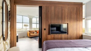 A modern bedroom with a large bed, a TV mounted on a wooden wall, and a view of the city through large windows. - comfortable apartment with panoramic views (Den Haag)