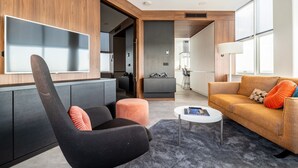 A modern living room with a sofa, armchair, and coffee table. There is a TV mounted on the wall, and a kitchen area is visible in the background. - comfortable apartment with panoramic views (Den Haag)