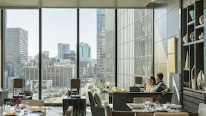Un comedor moderno con amplios ventanales que ofrecen vistas a la ciudad, muebles contemporáneos y un diseño limpio y minimalista.