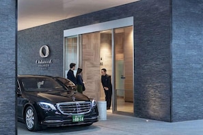 Entrada de un edificio moderno con un coche negro estacionado afuera, un cartel que dice 'Oshawa Premier' y una puerta de vidrio que da al interior.