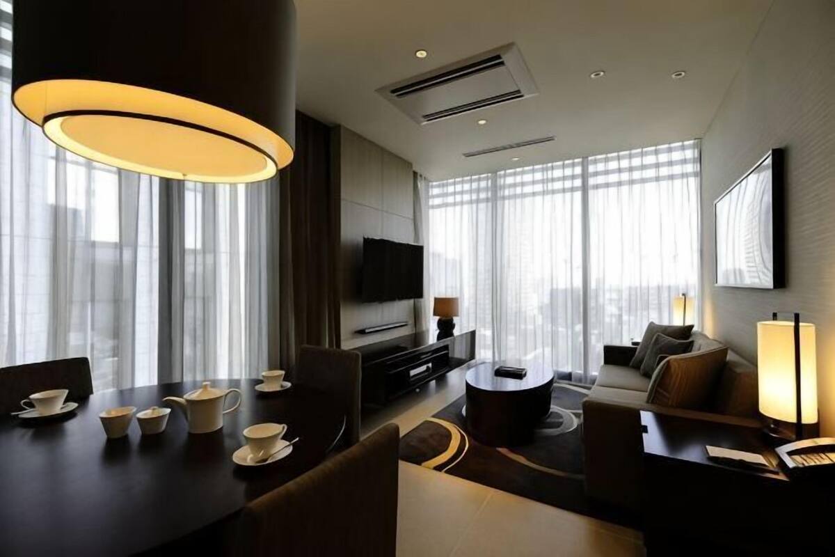 Une chambre d’hôtel moderne dotée d’un coin repas, d’un canapé, d’une télévision et de grandes fenêtres.