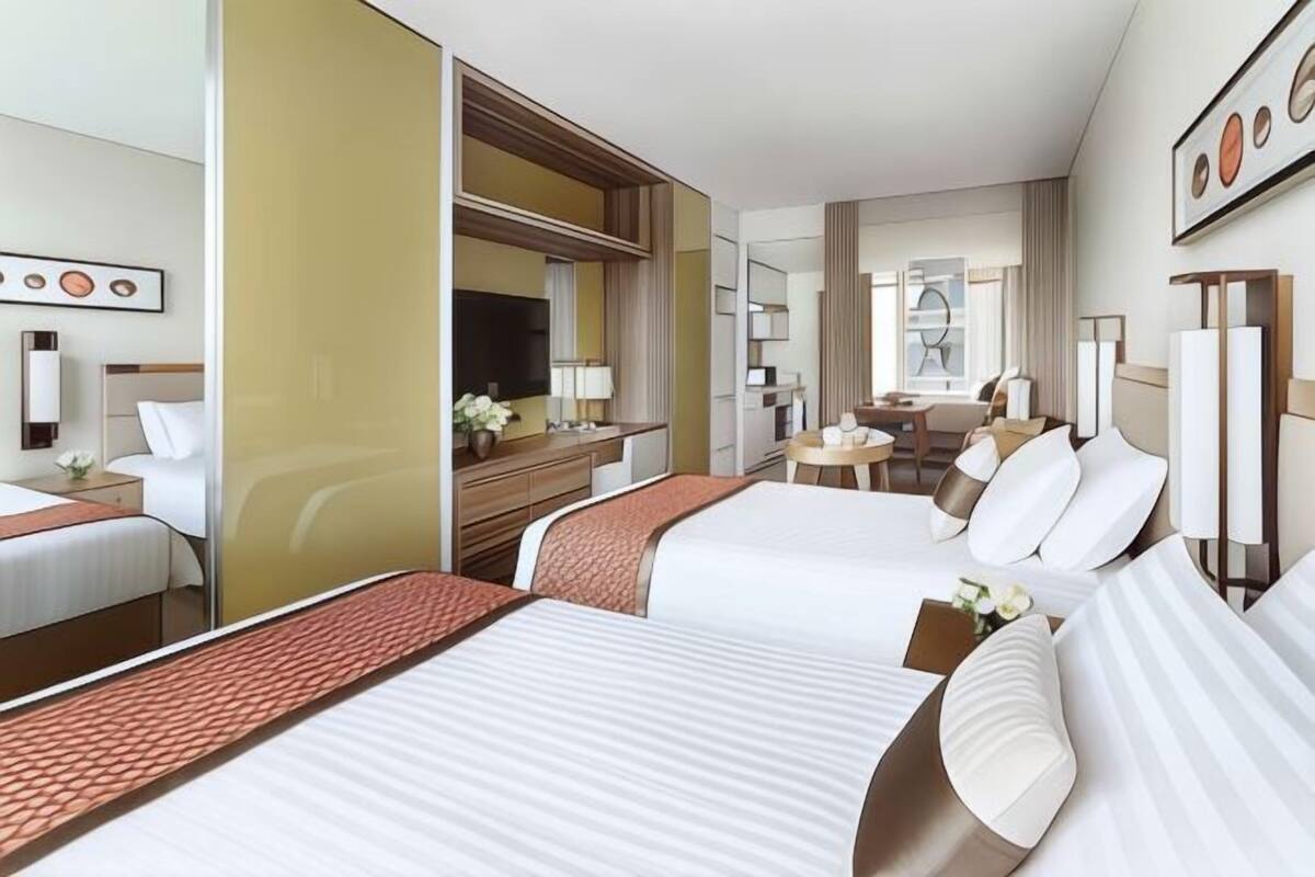 Une chambre d’hôtel avec deux lits, un bureau, une chaise, une télévision et un grand miroir.