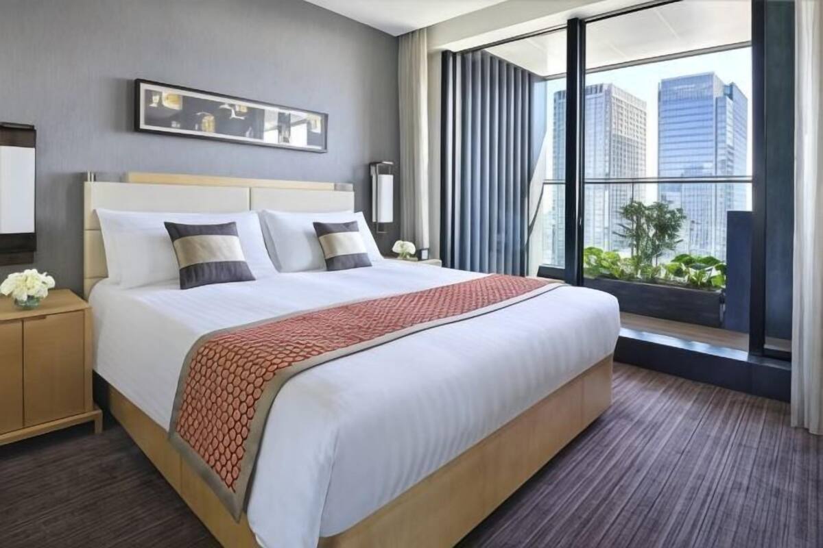 Une chambre d’hôtel avec un grand lit, une table de chevet, une fenêtre donnant sur la ville et un tableau encadré au mur.