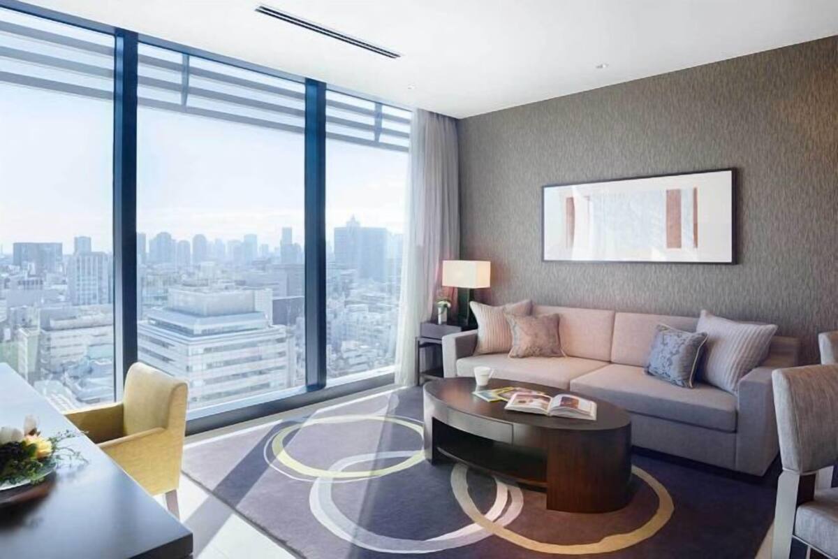 Un salon moderne avec un canapé, une table basse et une vue sur la ville grâce à de grandes fenêtres.