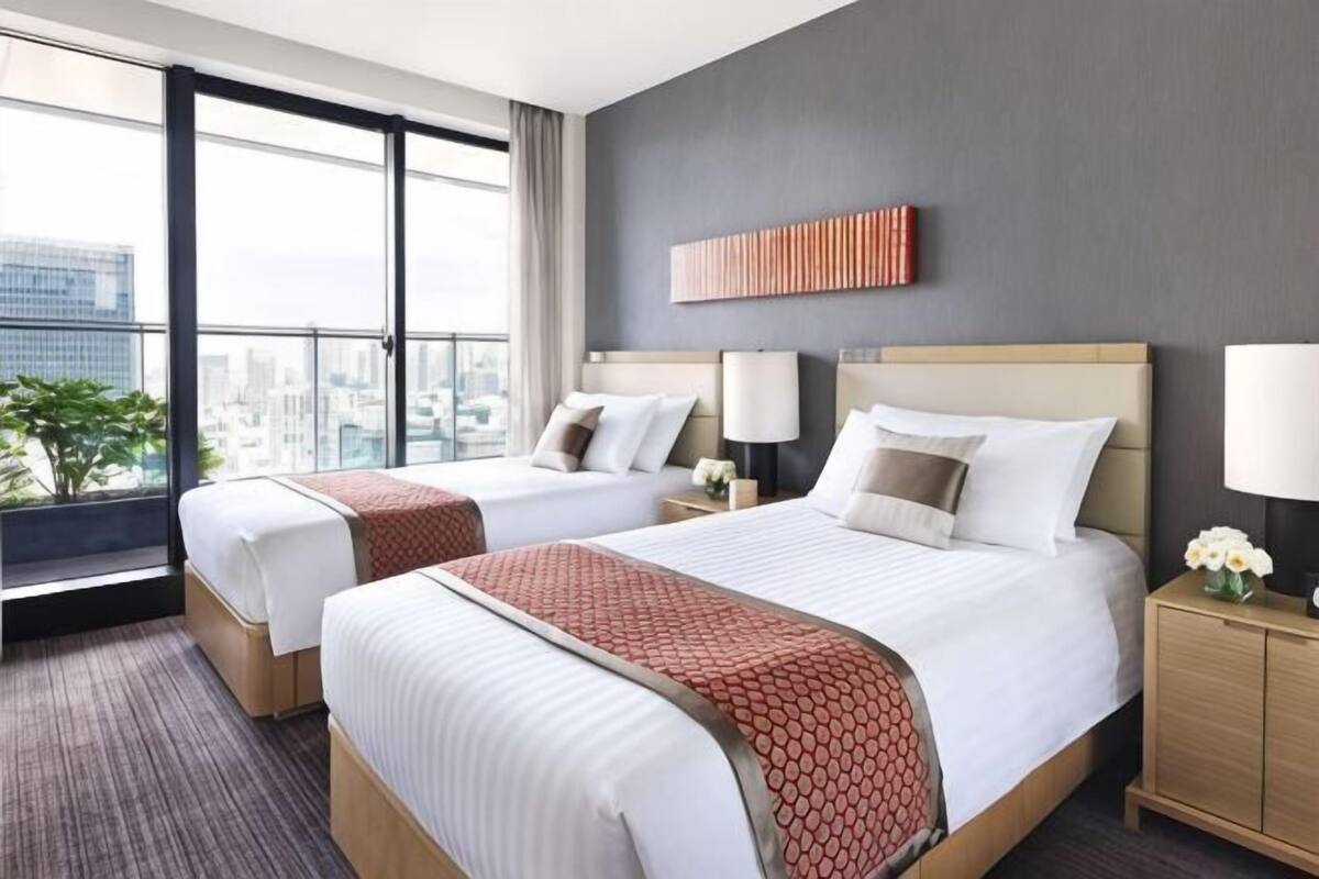 Une chambre d’hôtel avec deux lits, une vue sur la ville, un design moderne et une table de chevet avec une lampe.
