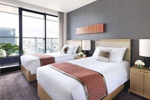 Habitación de hotel con dos camas, vista a la ciudad, diseño moderno y una mesita de noche con lámpara.