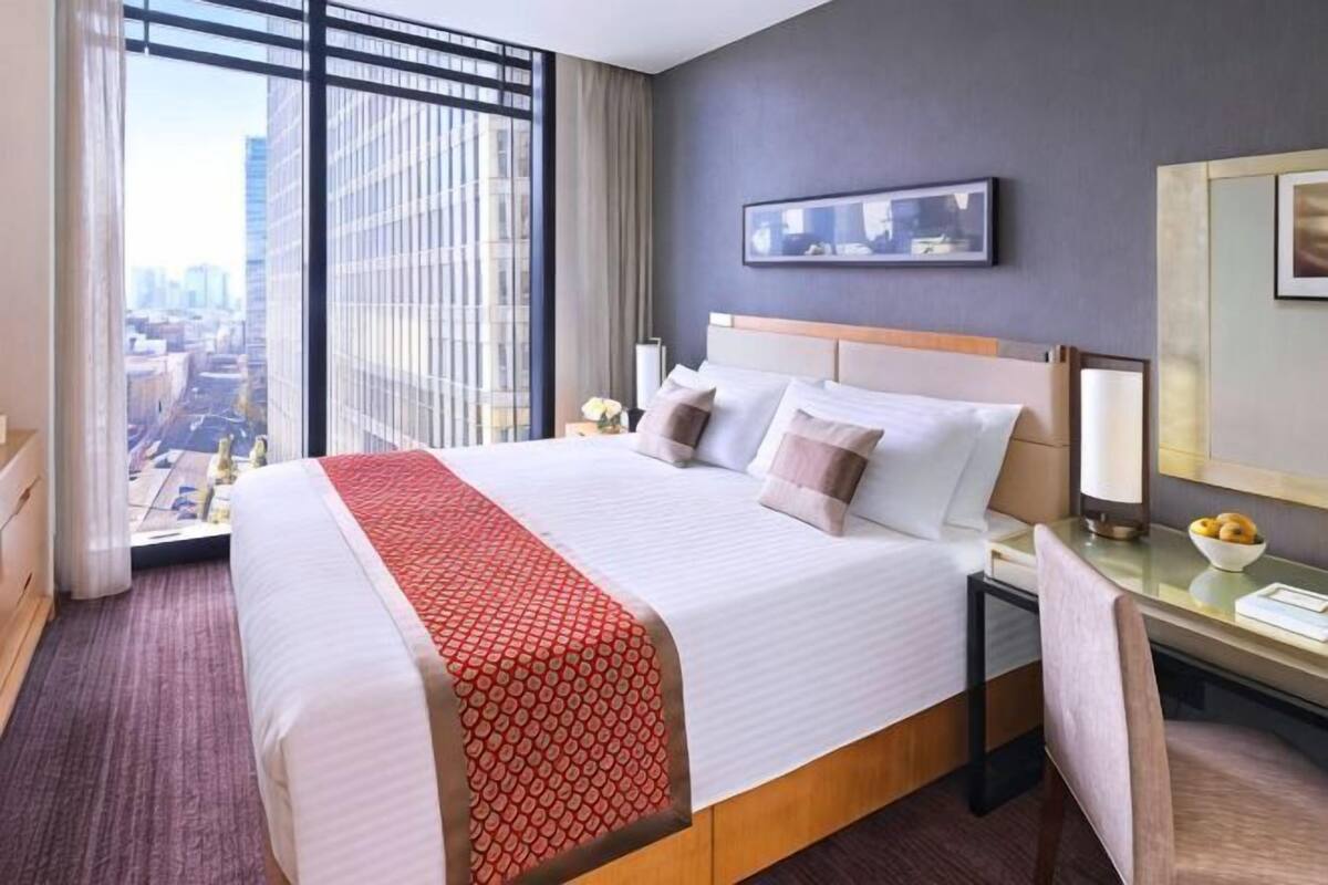 Une chambre d’hôtel avec un grand lit, un bureau, une chaise, une table de chevet, une lampe et une vue sur la ville.