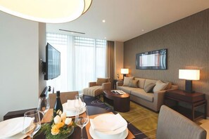 A hotel room with a dining area, a sofa, a TV, and a large window. - Oakwood Premier Tokyo (Tokyo)