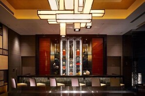Un moderno vestíbulo de hotel con una larga mesa de recepción, asientos y un separador de vidrio decorativo.