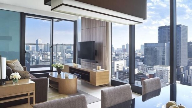 Una sala de estar moderna con un televisor grande, asientos cómodos, una mesa de centro y vistas a la ciudad.
