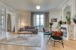 A spacious living room with a grey sofa, a wooden coffee table, and a dining area with a marble fireplace.