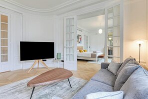 A modern living room with a flat-screen TV, a wooden coffee table, a grey sofa, and a large window.