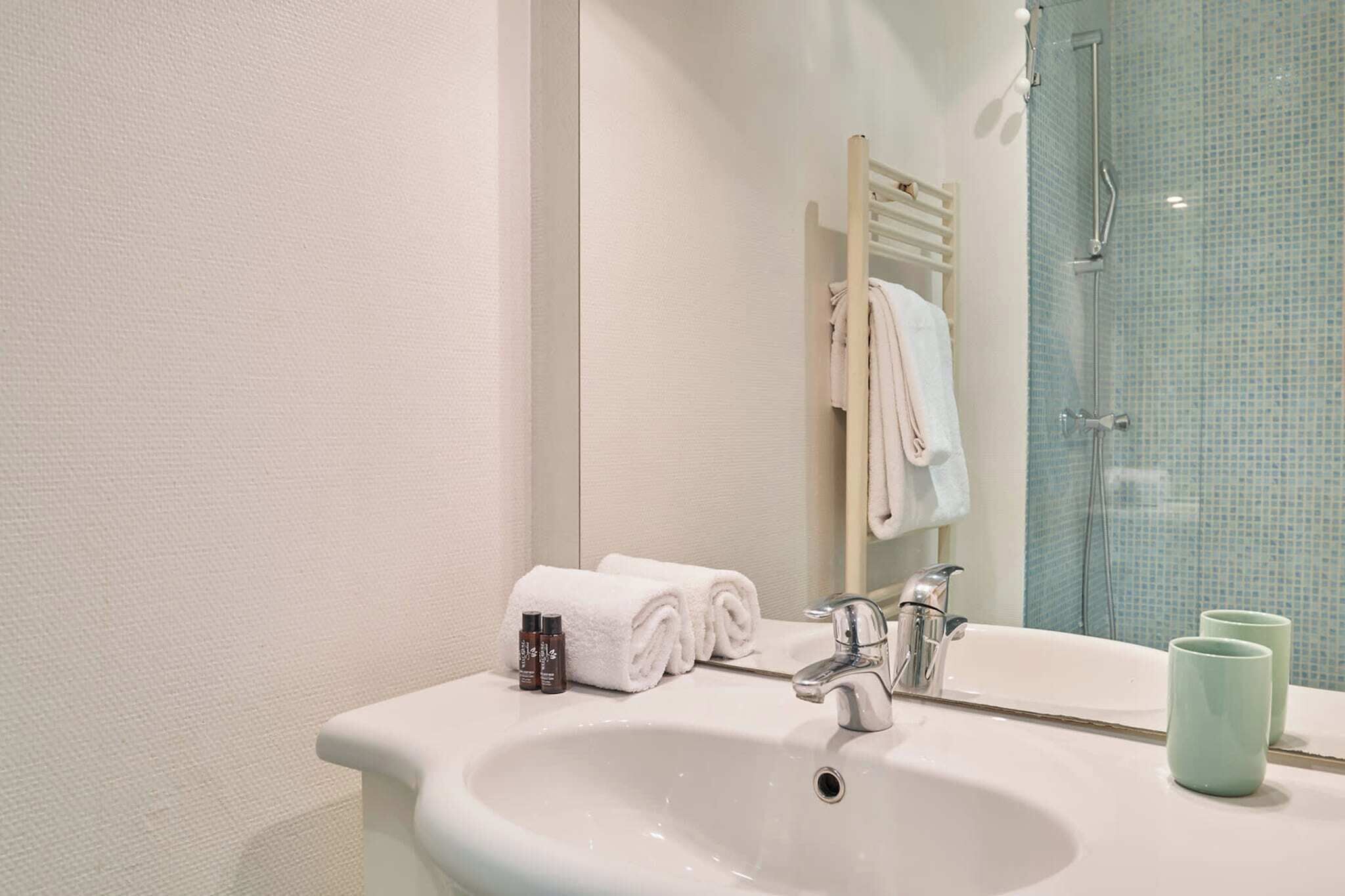 Une salle de bain avec un lavabo blanc, un miroir et une cabine de douche en verre.