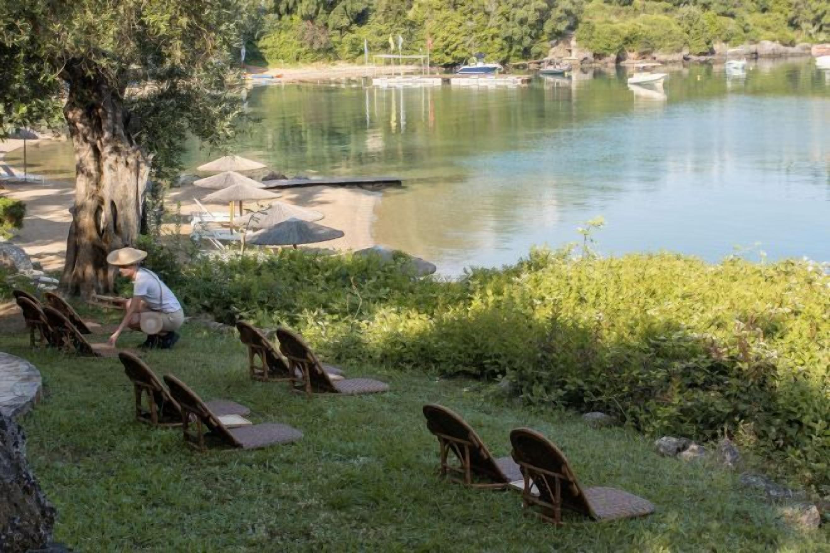 Un espacio de descanso junto al lago con sillas y sombrillas, un árbol y una masa de agua tranquila.