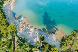 An aerial view of a beach with rows of umbrellas and sun loungers along the shoreline. - Grecotel Eva Palace (Limni)