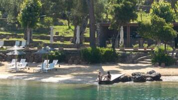 A pool area with lounge chairs and umbrellas, surrounded by trees and a stone wall.