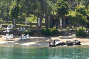 A pool area with lounge chairs and umbrellas, surrounded by trees and a stone wall. - Grecotel Eva Palace (Limni)