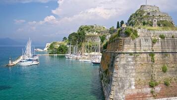 A coastal scene with a fortified structure, boats, and a clear sky.