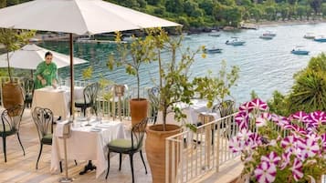 An outdoor dining area with tables and chairs, overlooking a body of water with boats.